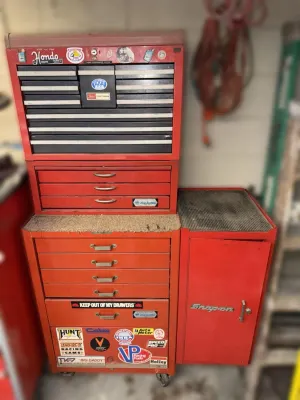Vintage red Craftsman and Snap-on rolling tool chest stack, showing heavy use and adorned with various automotive and racing stickers.