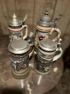Collection of four vintage German beer steins featuring detailed relief illustrations and pewter lids.