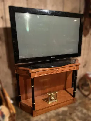 Samsung flat-screen television on a traditional wooden media console with black and gold column accents, featuring a brass mantel clock...
