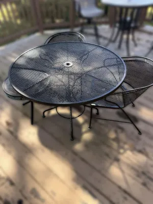 Vintage black wrought iron patio set featuring a round mesh-top table with an umbrella hole and three matching mesh barrel chairs.