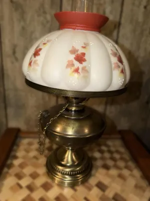 Vintage hurricane-style electric table lamp featuring a brass base and a white milk glass shade decorated with autumn maple leaves.