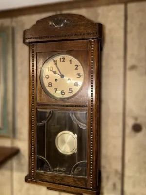 Vintage oak regulator wall clock featuring a carved crest, beaded trim, and a leaded glass lower door showcasing the brass pendulum.