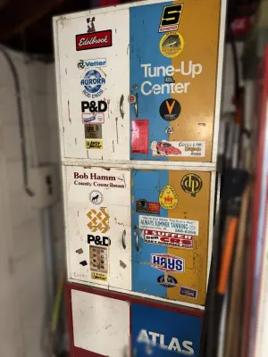 Vintage metal garage storage cabinet featuring a "Tune-Up Center" graphic and various automotive and novelty decals, showing...
