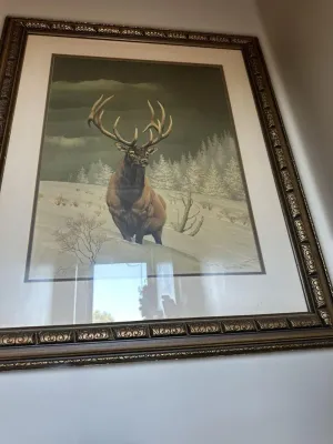 Framed wildlife art print depicting a bull elk in a snowy winter landscape, housed in an ornate, dark-finished frame with gold accents.