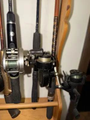 Assorted vintage fishing rods and reels, including baitcasting and spinning models, displayed on a wooden storage rack.