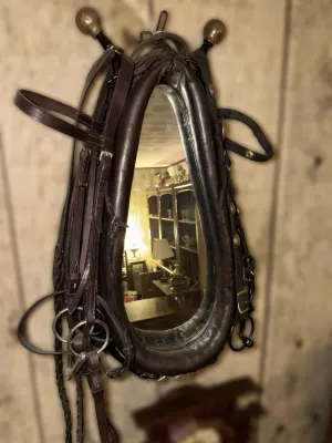 Vintage horse collar mirror featuring dark leather padding, brass hames, and attached bridle straps.