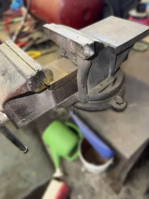 Heavy-duty cast iron bench vise with integrated anvil, showing signs of workshop use and wear.