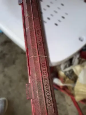 Red plastic protective case for a click-type torque wrench, showing some wear and dust from garage storage.