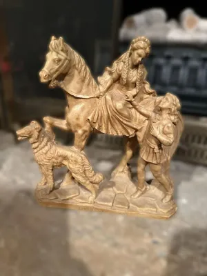 Vintage chalkware or plaster statue depicting a woman on horseback, a man, and a dog, finished in a gold-tone paint.
