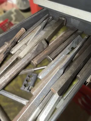 Assortment of vintage metal chisels and punches in a toolbox drawer, showing signs of use and wear.