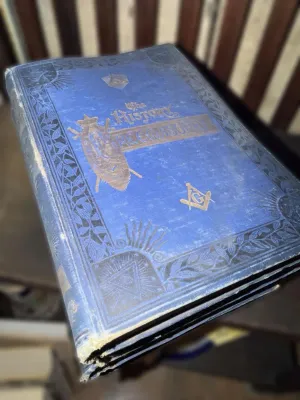 Antique copy of "The History of Freemasonry" featuring a blue cloth cover with ornate gold and black embossed Masonic symbols,...