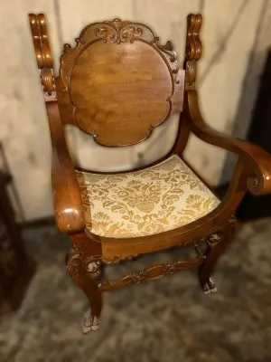 Antique carved wood armchair featuring a decorative crest, curved armrests, and a gold damask upholstered seat.