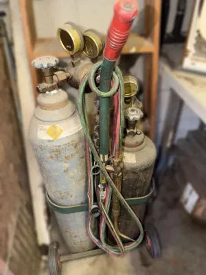 Vintage oxy-acetylene welding torch set on a wheeled cart, featuring dual tanks with regulators, hoses, and a torch handle.