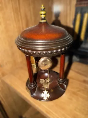 Vintage wooden pocket watch stand with a domed top and beaded trim, displaying a gold-tone pocket watch and a decorative fob.