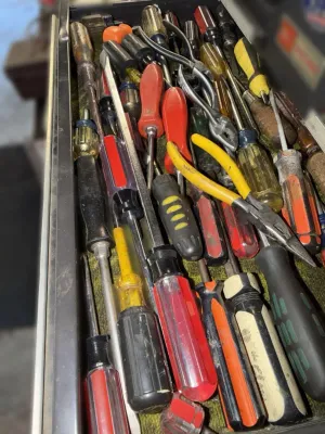 Assorted vintage and modern hand tools, including various screwdrivers and pliers, stored in a metal toolbox drawer.