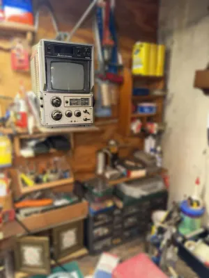 Vintage MGA Mitsubishi portable television and radio unit, showing some wear from age and use, set against a cluttered workshop background.