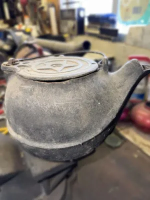 Antique cast iron tea kettle featuring a star design on the lid, showing a dusty, weathered patina.