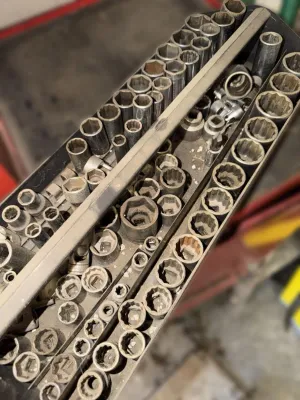 Assorted collection of dusty, used socket wrench attachments organized in a black plastic tray.