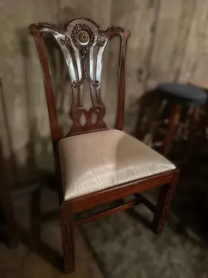 Chippendale-style mahogany dining chair featuring an ornate carved splat with a central medallion and a light-colored upholstered seat.