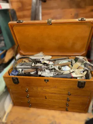 Vintage wooden machinist chest with a top compartment and multiple drawers, filled with various hand tools including pliers, wrenches,...