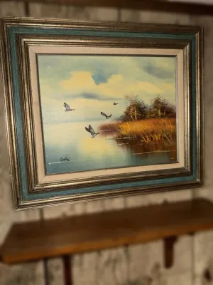 Vintage oil painting depicting ducks flying over a marshy lake, housed in an ornate gold and teal wooden frame.
