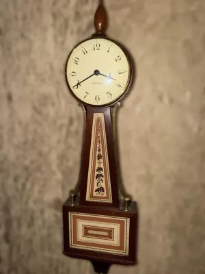 Seth Thomas banjo wall clock featuring a wooden case with decorative painted panels and a brass finial.