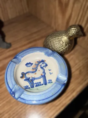 Small hand-painted ceramic ashtray featuring a blue horse motif, paired with a vintage brass quail figurine.