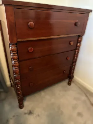 Antique Empire-style mahogany chest of drawers featuring four spacious drawers with wooden knobs and decorative spool-turned side columns.