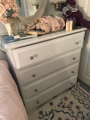 White-painted wooden four-drawer dresser with simple silver-toned knobs, shown with various decorative items on top.