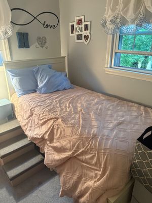 Twin-size wooden bed frame with a white headboard, dressed in a textured pink comforter and light blue pillows, accompanied by a set of...