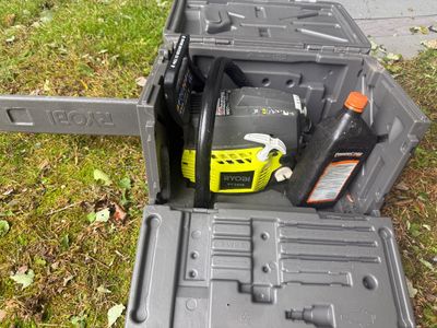 Ryobi RY3818 gas-powered chainsaw with a protective scabbard, housed in its original grey plastic carrying case alongside a bottle of...