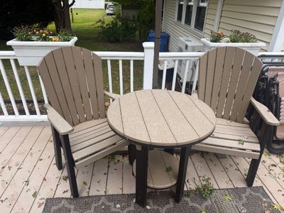 Three-piece outdoor patio set featuring two tan and black composite Adirondack chairs and a matching round side table.