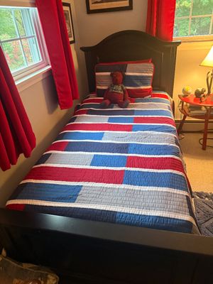 Dark wood twin-size bed frame with a matching headboard, dressed in a red, white, and blue patchwork quilt with a matching pillow sham.
