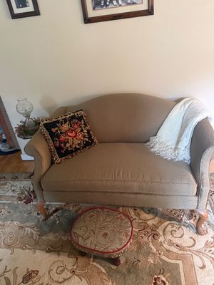 Traditional camelback loveseat with patterned beige upholstery and cabriole legs, paired with a small floral footstool, a needlepoint...