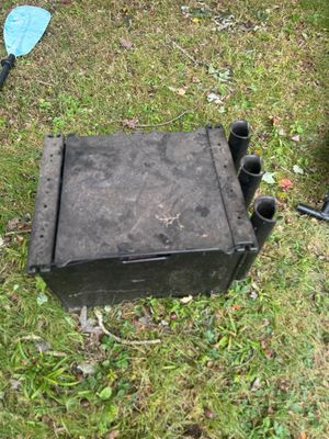 Black plastic kayak crate with integrated rod holders, showing some dirt and wear from outdoor use.