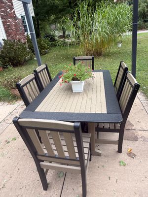 Polywood outdoor dining set featuring a rectangular table with a tan and black slatted top, accompanied by six matching high-back dining...