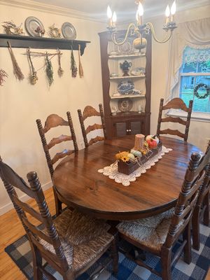 Rustic wooden dining set featuring an oval extension table and six ladder-back chairs with woven rush seats, shown alongside a matching...