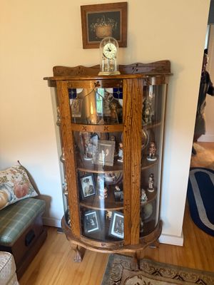 Antique oak bowfront china cabinet featuring curved glass sides, a stained glass accent panel, and claw-and-ball feet, filled with...