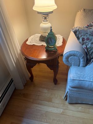 Traditional round wooden end table with cabriole legs, styled with a vintage-style green mantel clock and a ceramic table lamp on a lace...