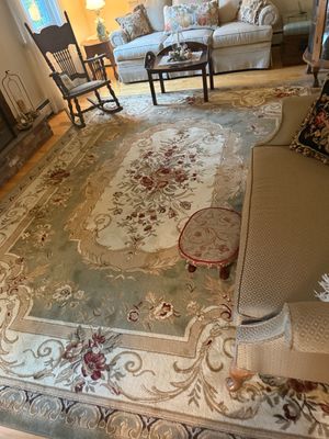 Large Aubusson-style area rug featuring a central floral medallion in shades of cream, sage green, and burgundy, shown in a living room...