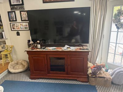 Large flat-screen television on a traditional cherry-finished wooden media console with a central glass door and flanking cabinets.