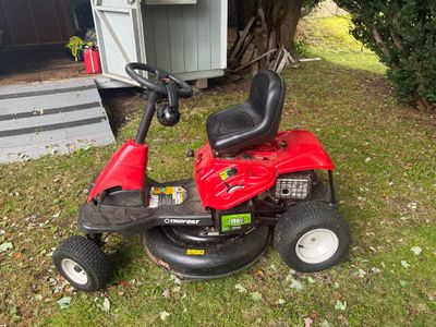 Troy-Bilt red riding lawn mower with a black seat and steering wheel, showing some wear from outdoor use.