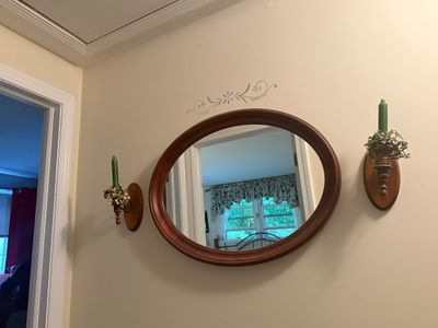 Vintage oval wall mirror with a cherry-finished wood frame, flanked by a pair of matching wooden candle sconces holding green taper candles.