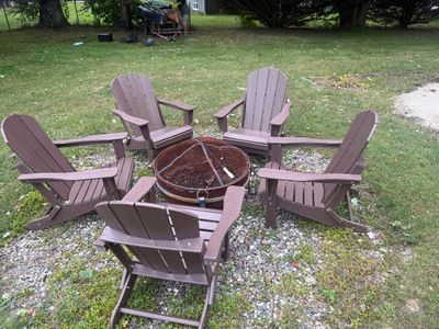 Set of five brown composite Adirondack chairs arranged around a round metal fire pit with a mesh spark screen.