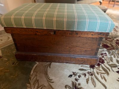 Vintage wooden storage bench featuring a rustic dark wood base and a padded top upholstered in a green and white plaid fabric.