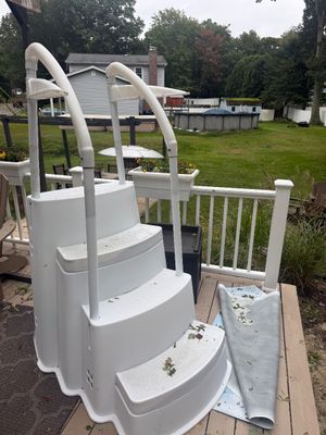 White molded plastic above-ground pool steps with dual handrails, showing some outdoor weathering.