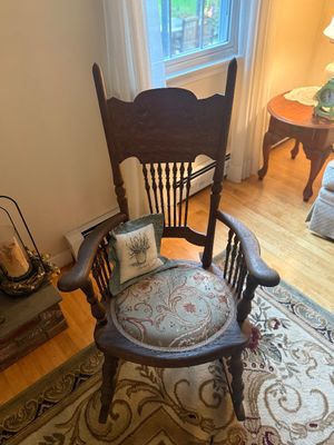 Antique carved oak rocking chair featuring a spindle back, curved armrests, and a round upholstered seat with a floral paisley pattern.