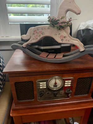 Vintage-style wooden tabletop rocking horse with hand-painted floral details, displayed atop a retro-style wooden radio and CD player...