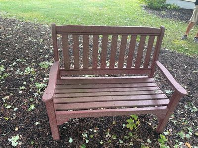 Reddish-brown composite lumber garden bench with a slatted seat and backrest, showing some light outdoor wear.