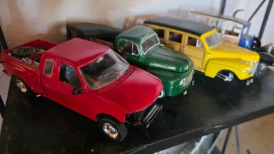 Collection of vintage and modern die-cast model trucks and cars, including a red pickup, a green classic truck, and a yellow woody wagon,...